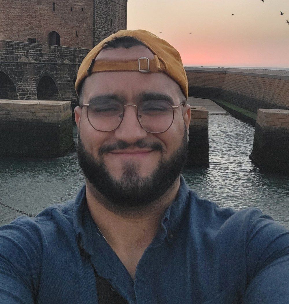 Omar smiling in a cap and glasses at sunset on the Essaouira ramparts